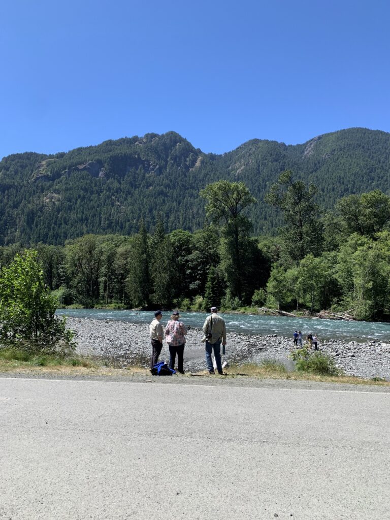 Three people standing on the side of a road next to a lake